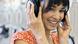 A woman an orange flower dress smiling about what she is hearing via her headphones